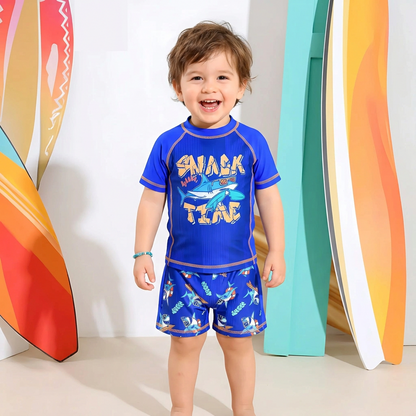 Child wearing a blue shark-themed swimsuit with colorful surfboards in the background